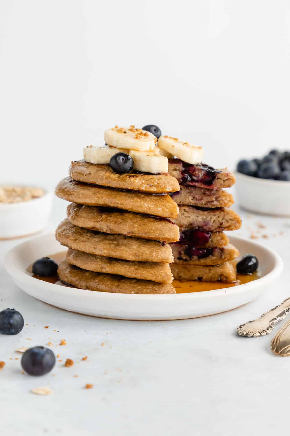 a stack of vegan gluten-free blueberry banana pancakes on a white plate with a portion cut out of it