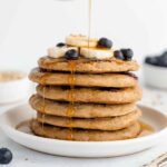 maple syrup being poured over a stack of vegan gluten-free blueberry banana pancakes