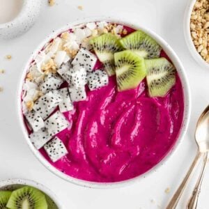 a dragon fruit smoothie bowl beside vintage spoons and bowls of fresh fruit