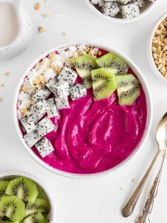 a dragon fruit smoothie bowl beside vintage spoons and bowls of fresh fruit