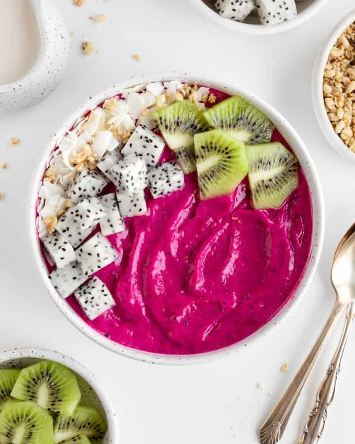 a dragon fruit smoothie bowl beside vintage spoons and bowls of fresh fruit