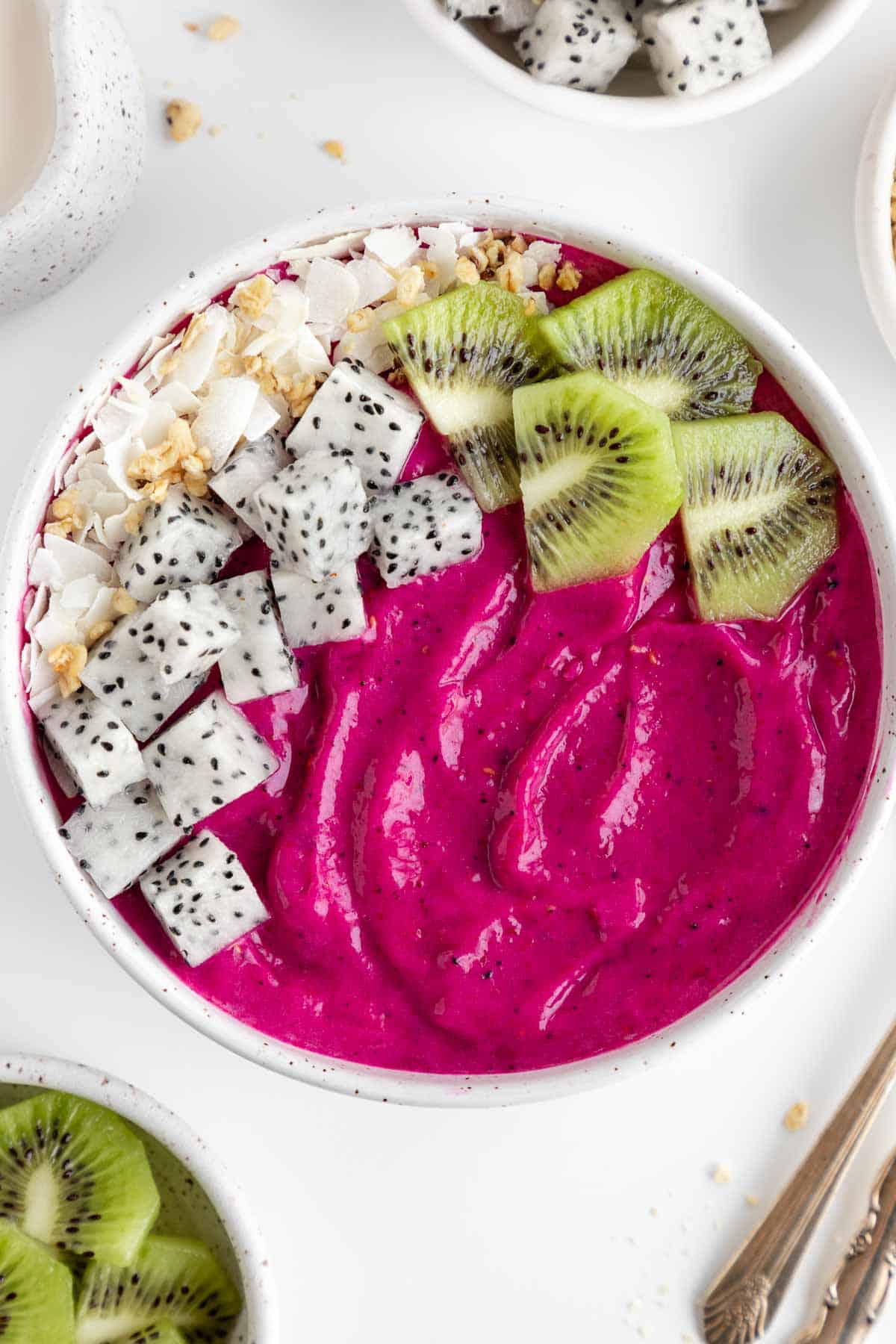 a dragon fruit smoothie bowl with coconut flakes, granola, kiwi, and pitaya on top