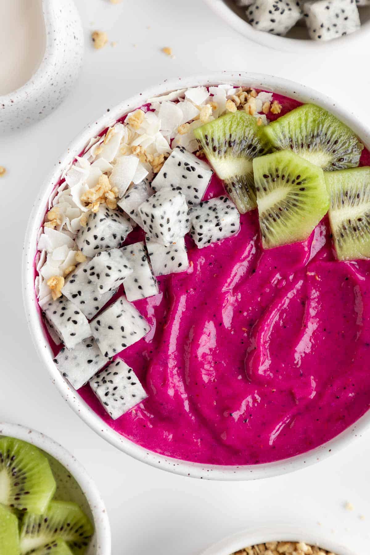 a dragon fruit smoothie bowl with coconut flakes, granola, pitaya, and kiwi on top