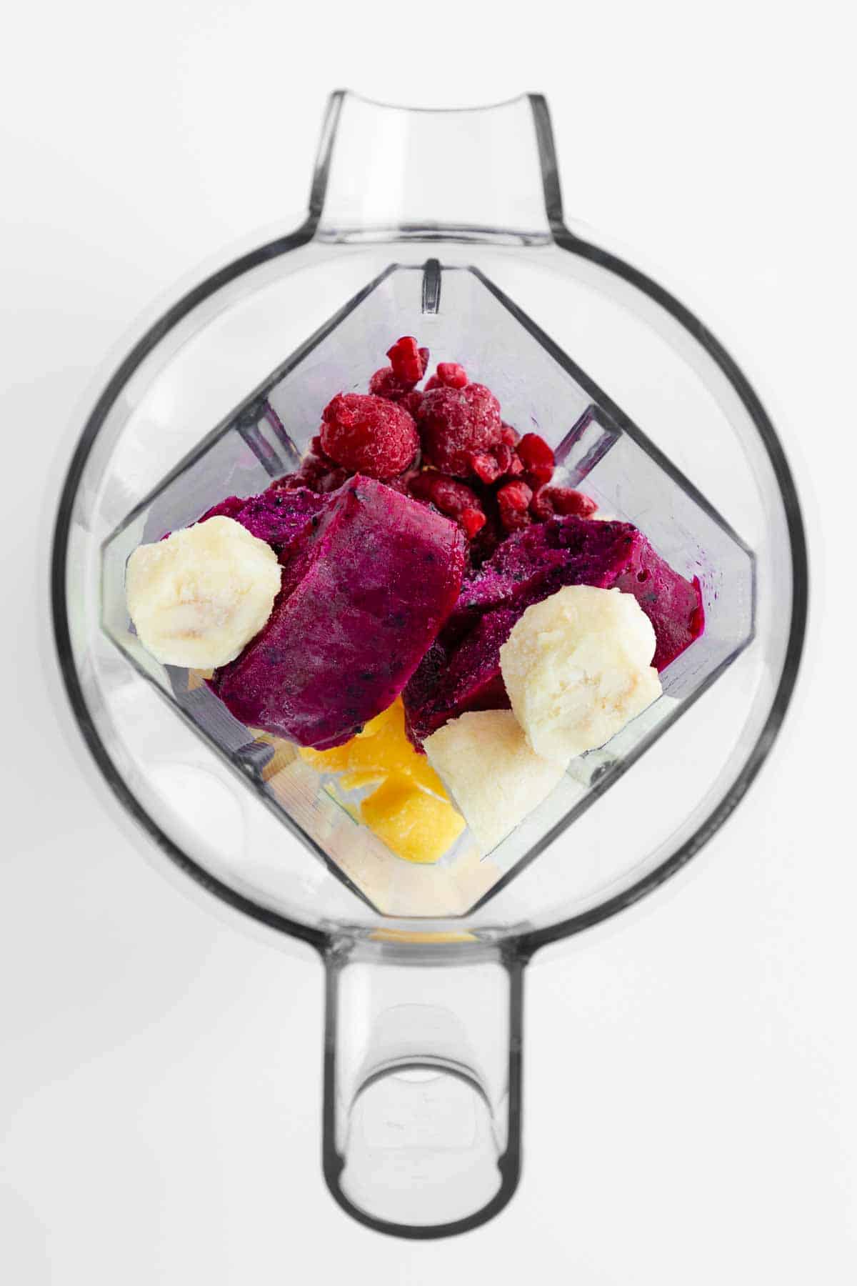 frozen pitaya packet, frozen bananas, mango chunks, and raspberries inside a vitamix blender
