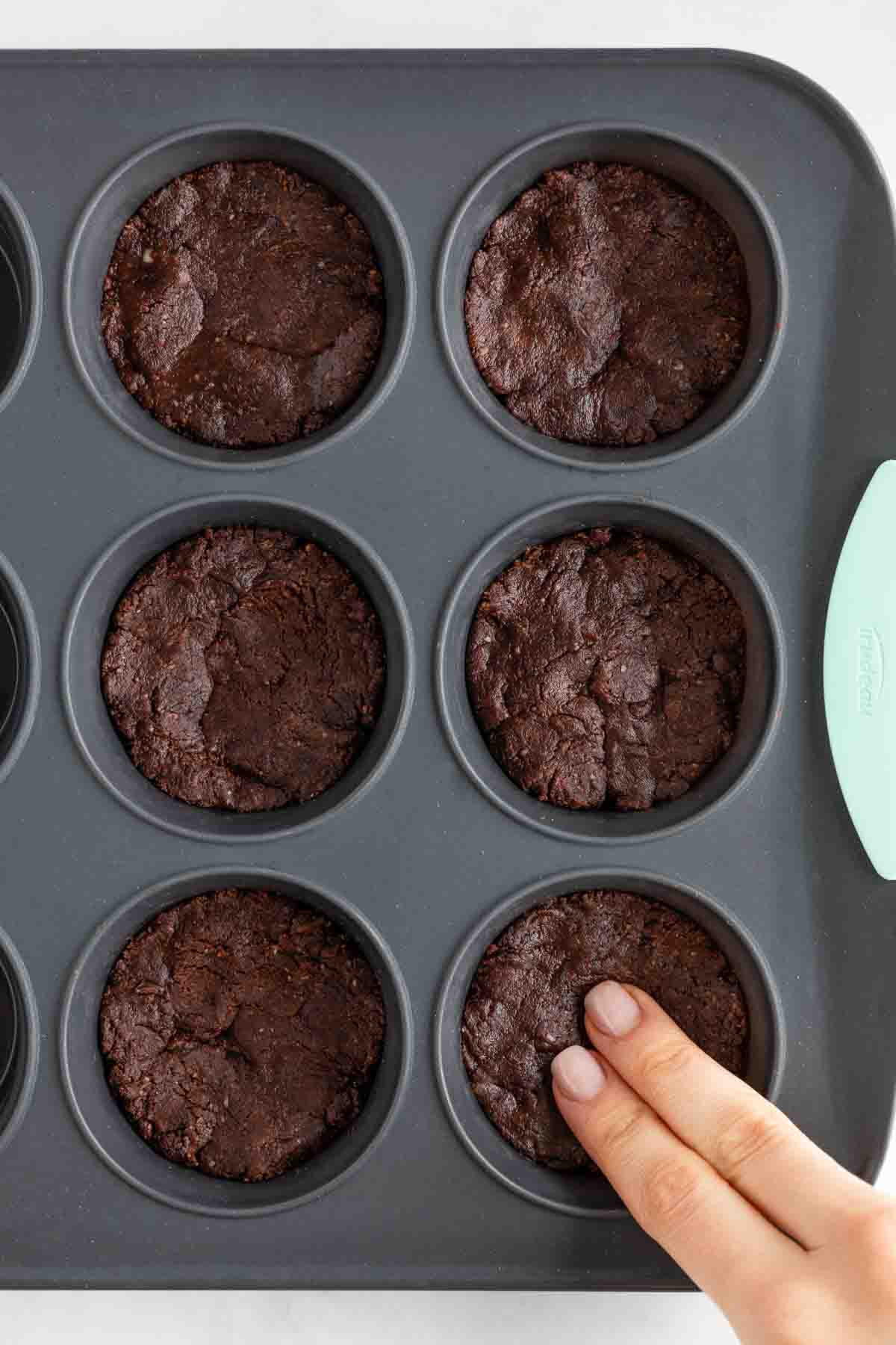 fingers pressing no bake brownie dough into a silicone muffin tin