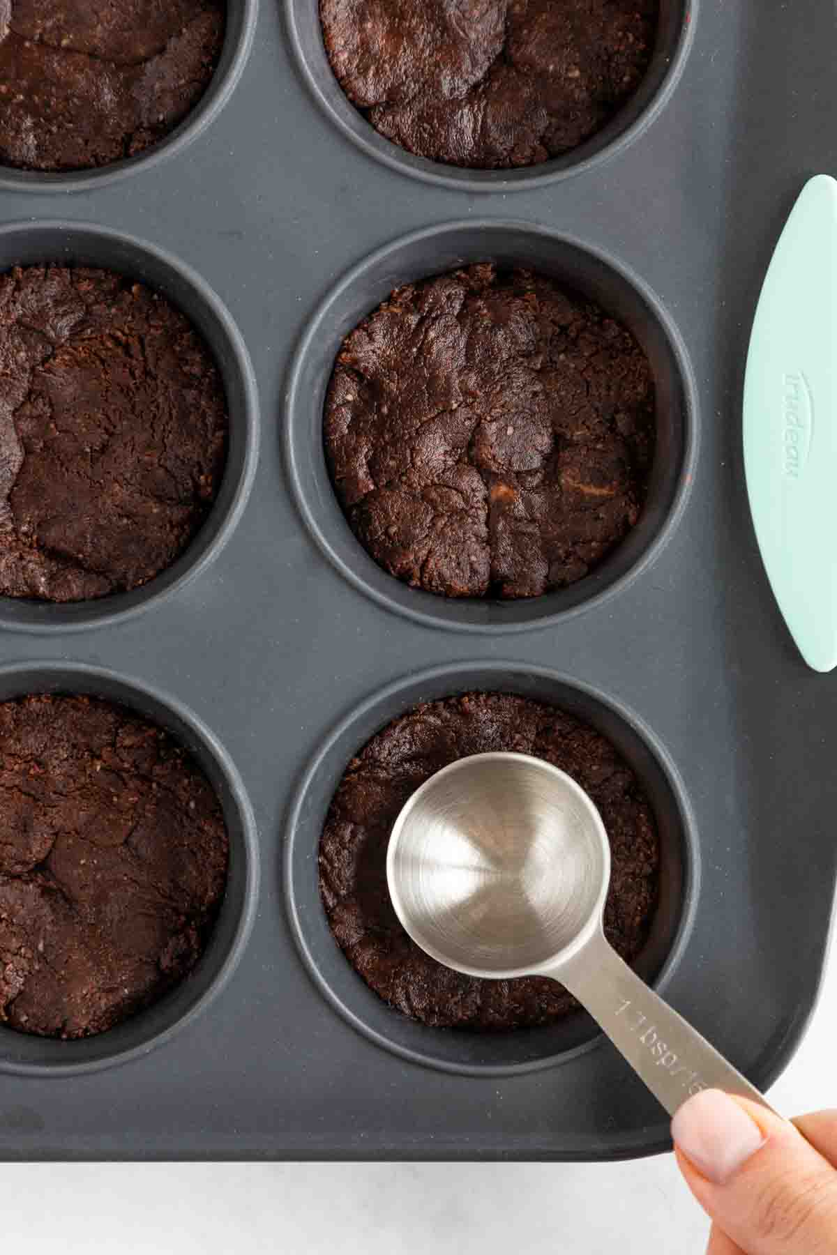 a tablespoon pressing into no bake brownies inside a muffin tin