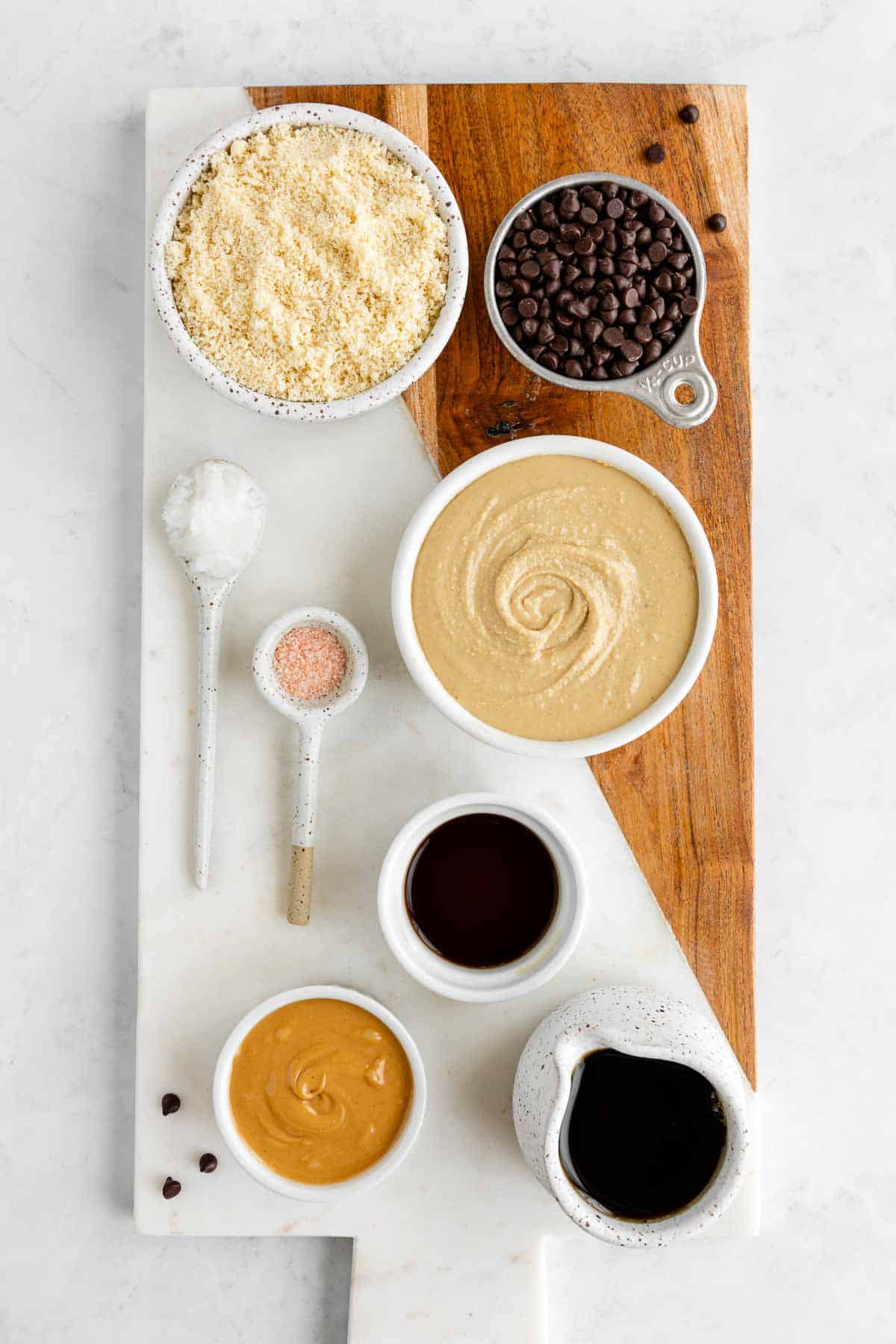 bowls of almond flour, cashew butter, maple syrup, chocolate chips, peanut butter, maple syrup, and vanilla extract on a marble serving board