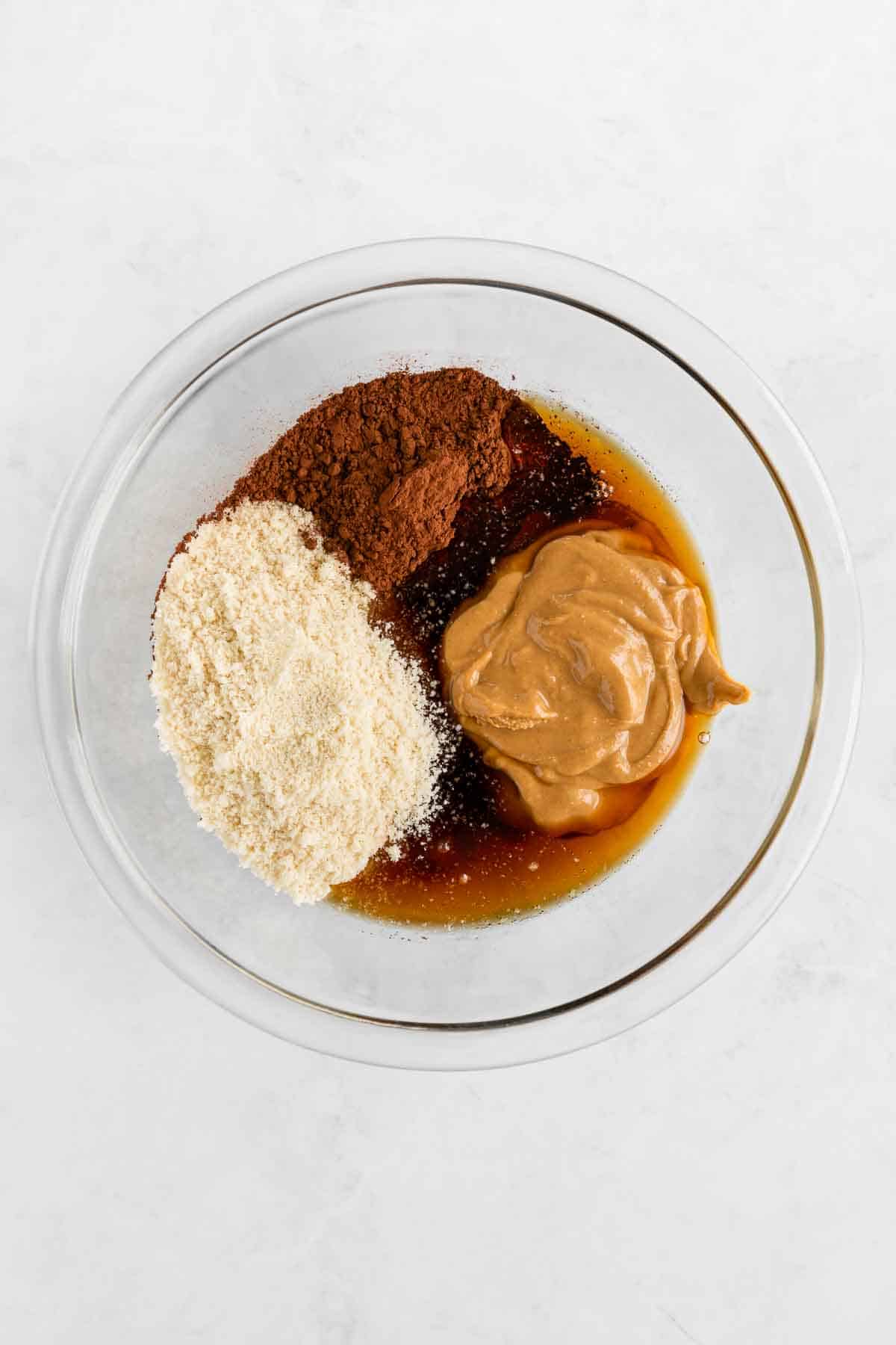 almond flour, peanut butter, cocoa powder, and maple syrup in a glass pyrex mixing bowl