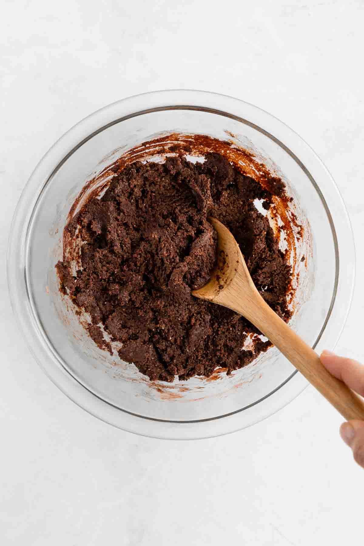 a wooden spoon mixing no bake brownie dough inside a glass bowl