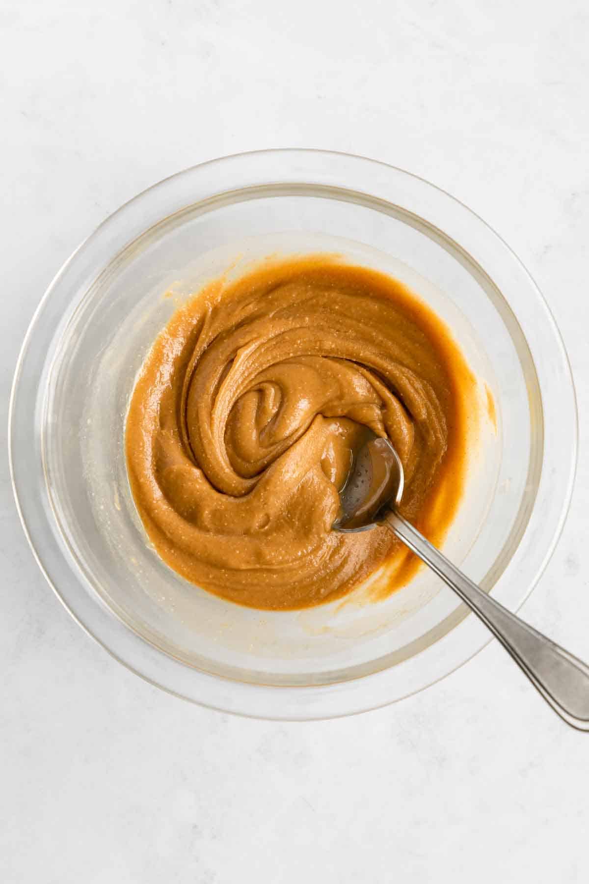 a spoon mixing peanut butter and maple syrup in a glass mixing bowl