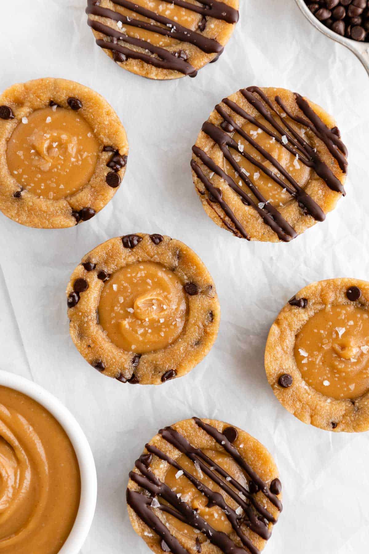 no bake caramel cookie dough cups on white parchment paper beside a bowl of chocolate chips