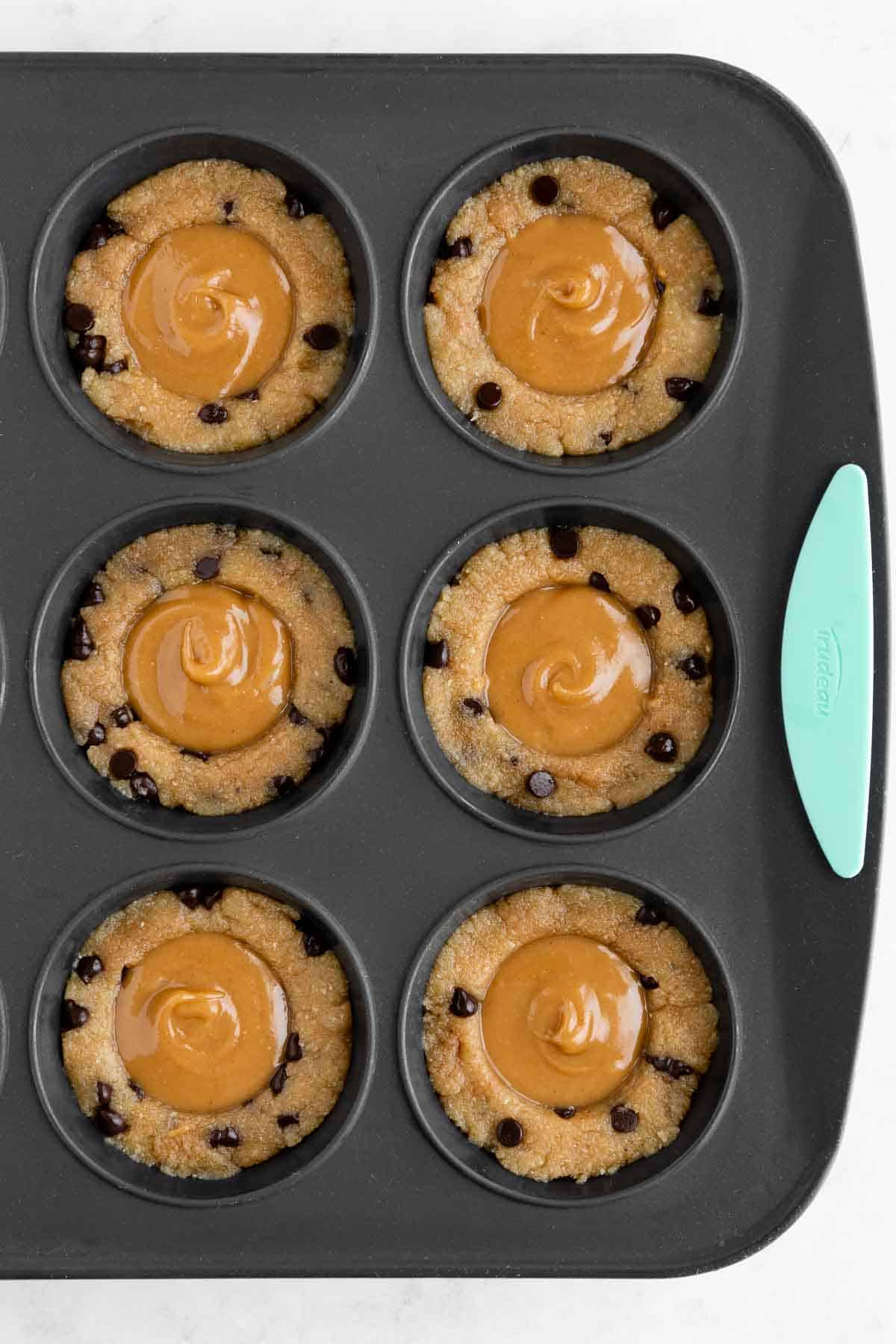 vegan cookie dough cups filled with caramel sauce in a silicone muffin pan