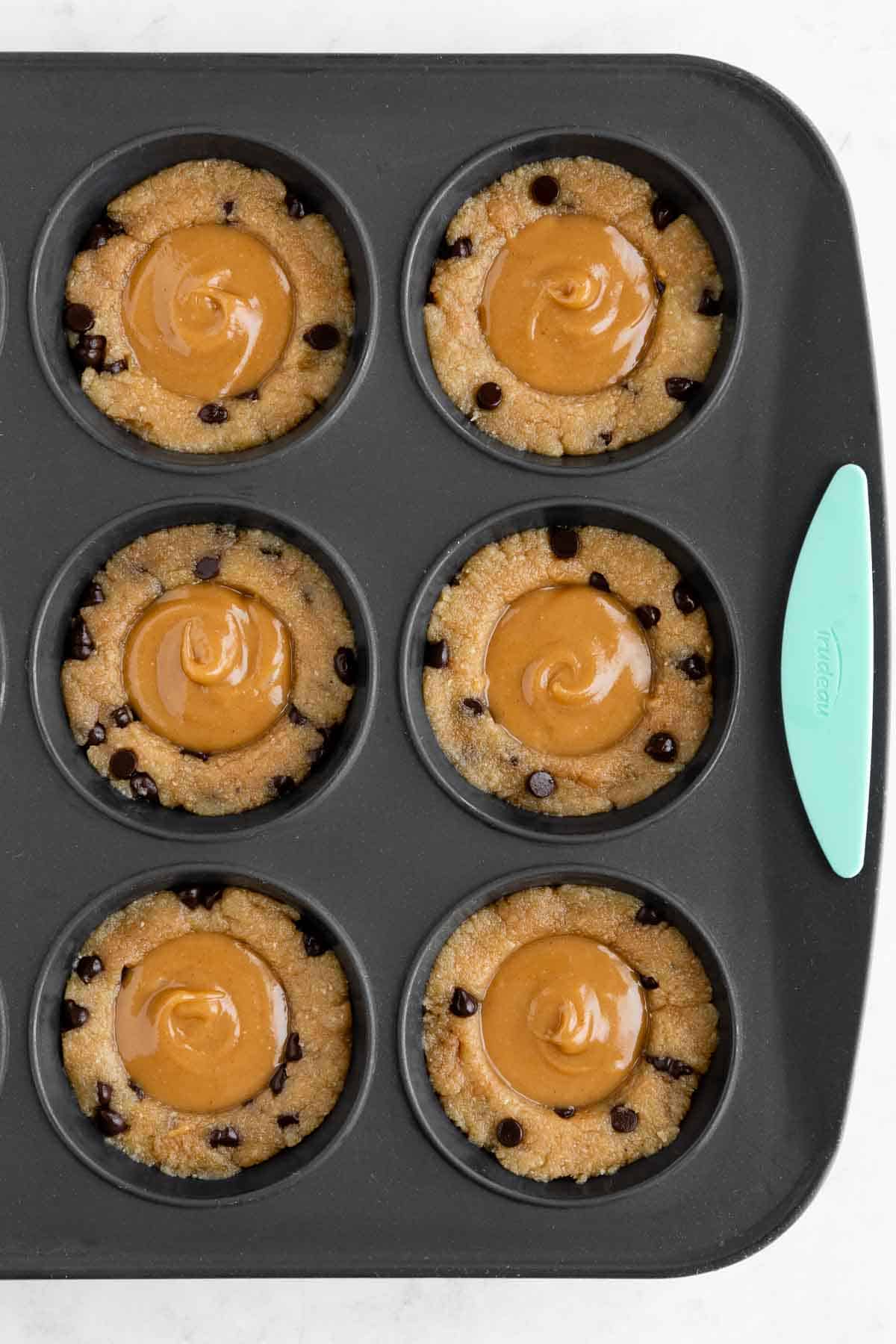 vegan cookie dough cups filled with caramel sauce in a silicone muffin pan