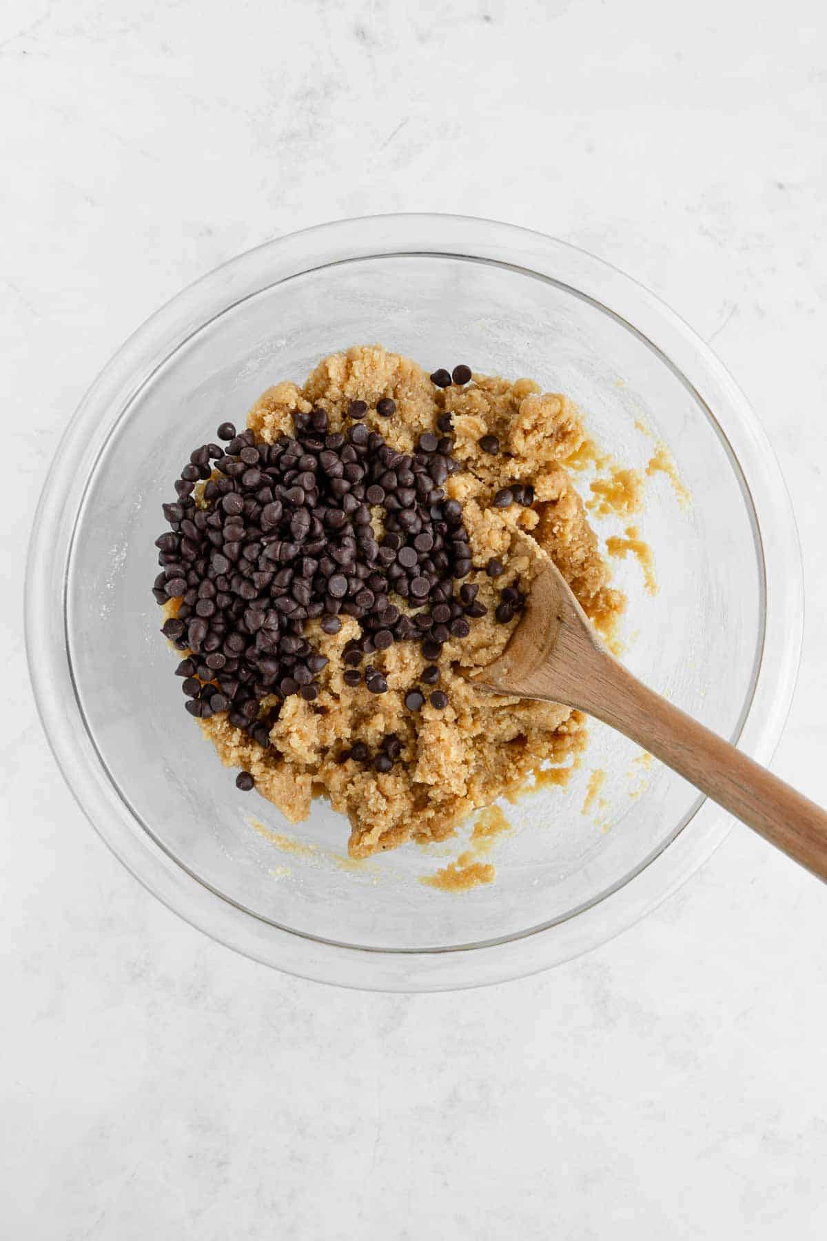 a wooden spoon mixing mini chocolate chips into vegan edible cookie dough