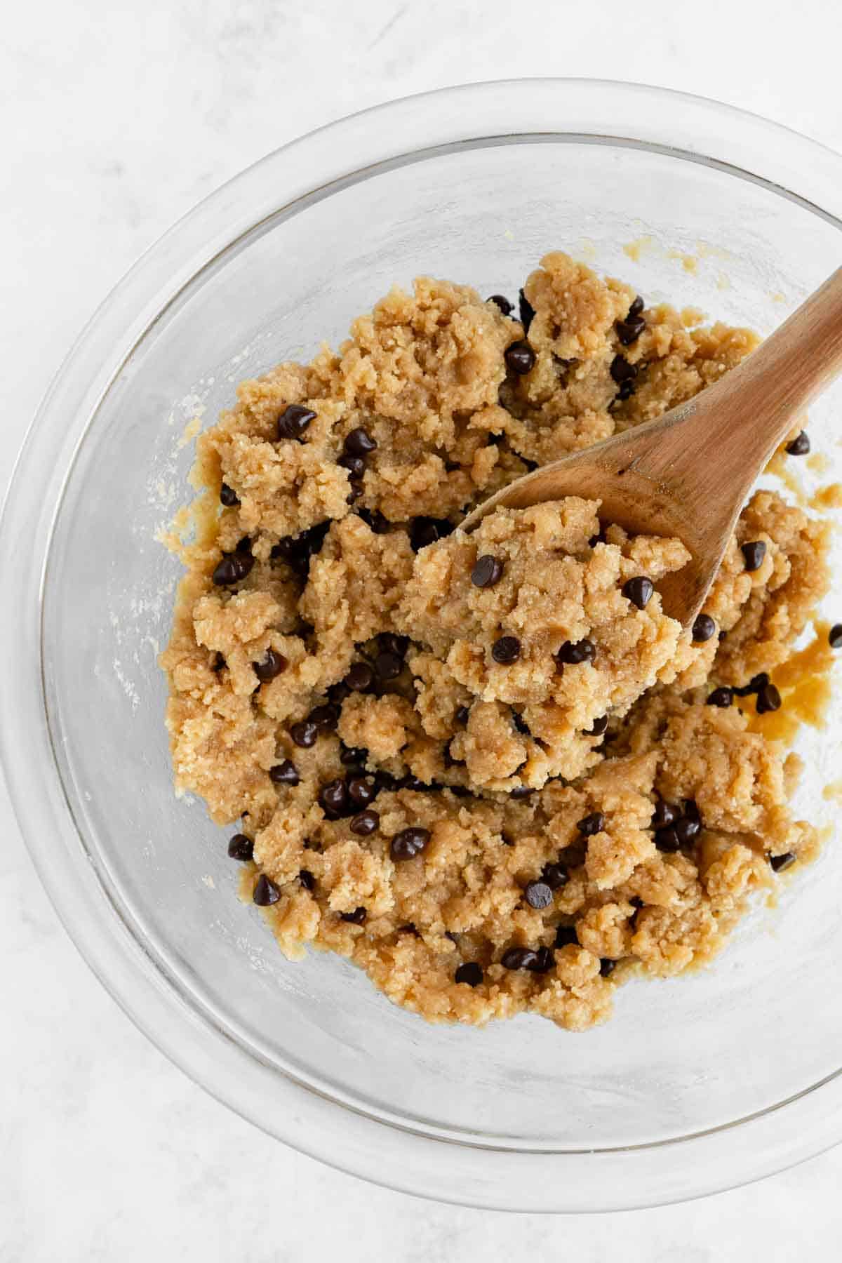 a wooden spoon scooping healthy edible cookie dough in a glass boiwl
