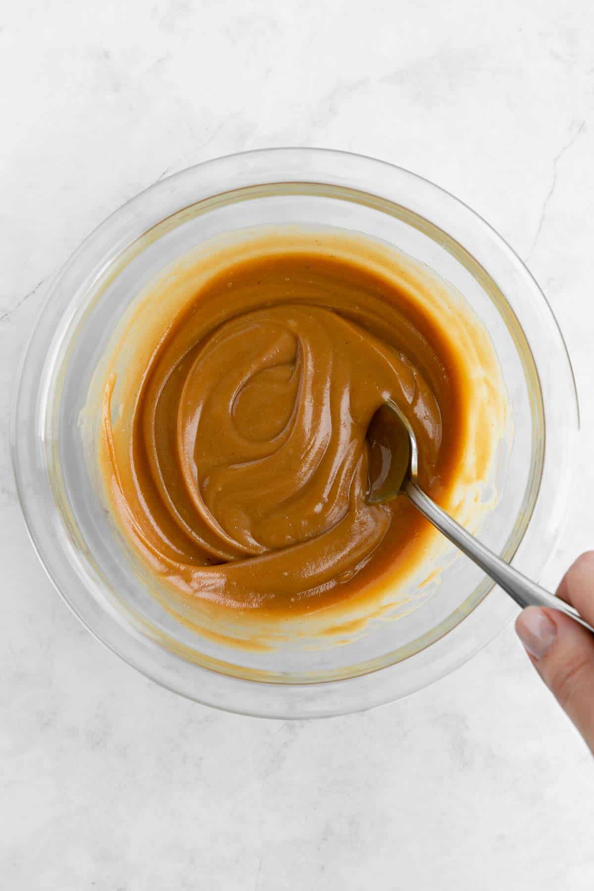 a spoon mixing vegan caramel in a glass bowl