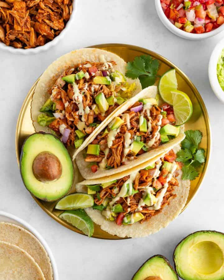 three vegan jackfruit tacos on a gold plate surrounded by ingredients