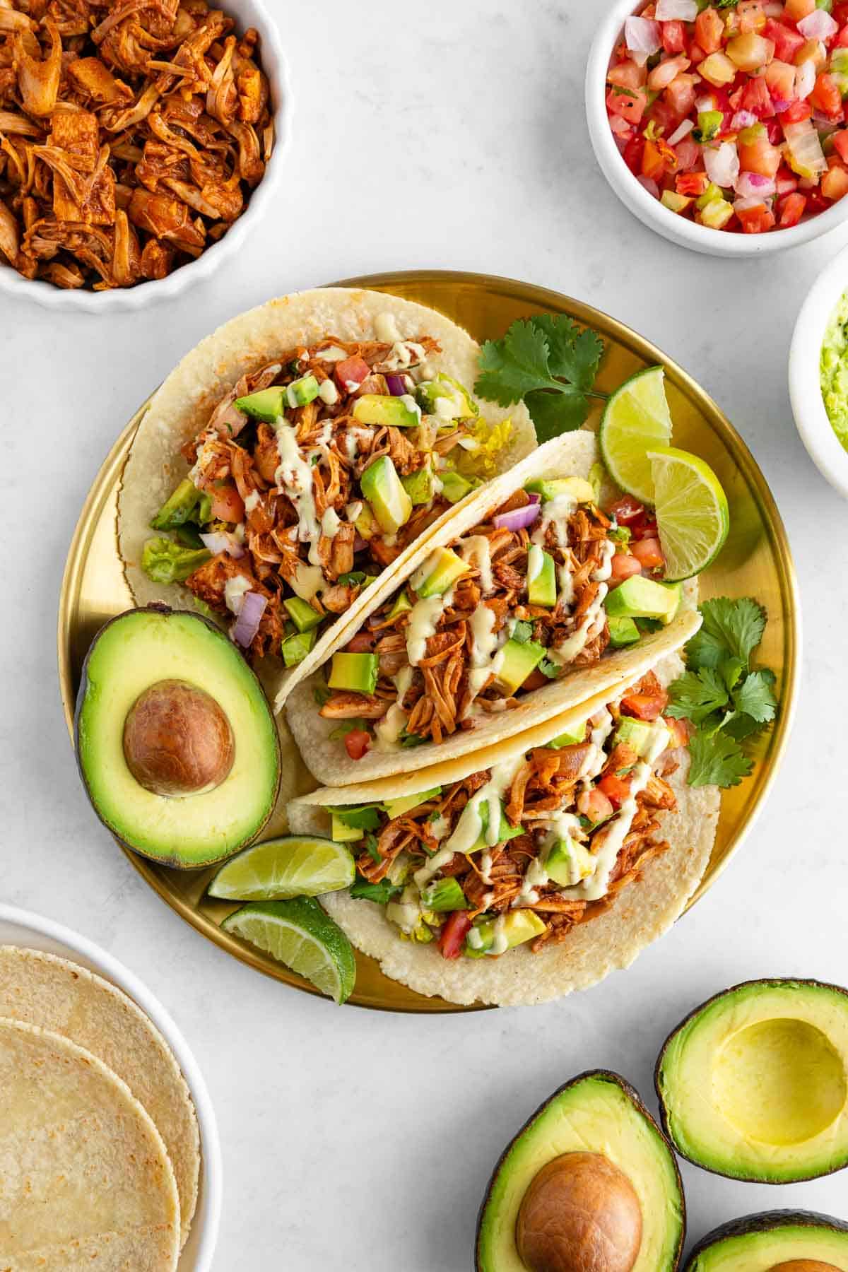 three vegan jackfruit tacos on a gold plate surrounded by ingredients