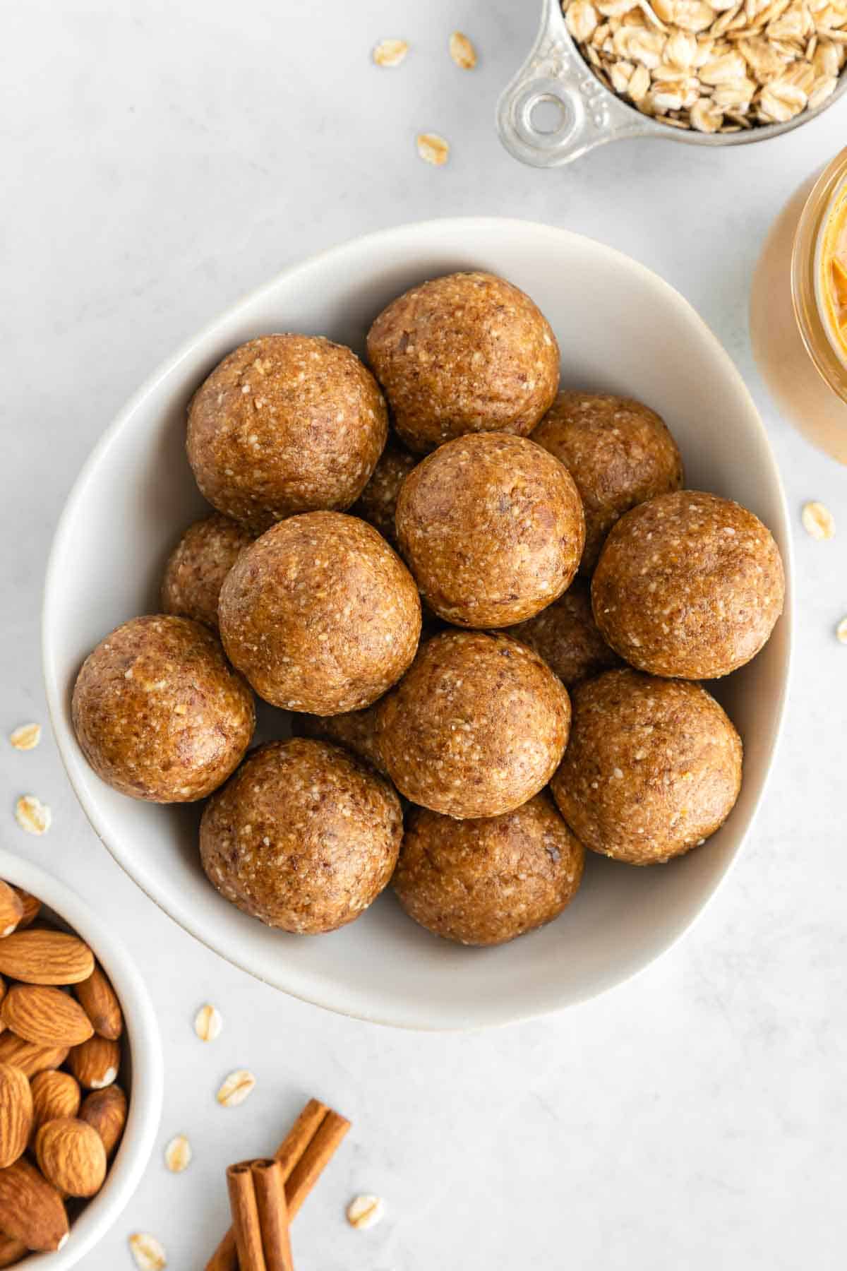 a bowl of almond butter energy balls beside almonds, rolled oats, and cinnamon sticks