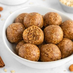 a white bowl filled with almond butter energy balls and a bite taken out of the middle one