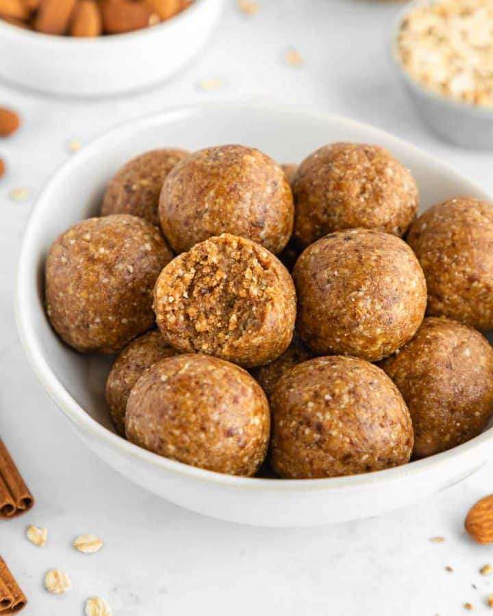 a white bowl filled with almond butter energy balls and a bite taken out of the middle one