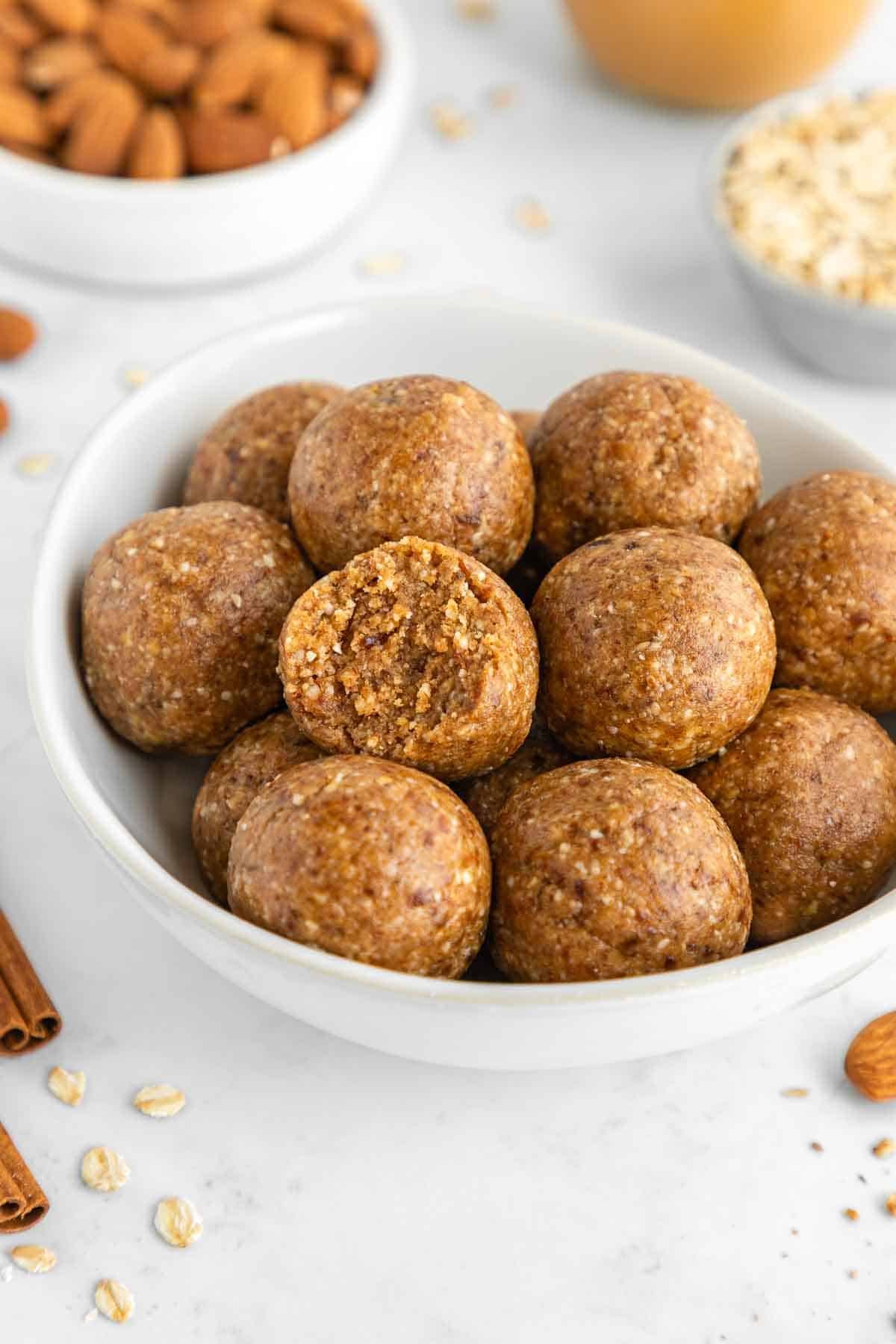 a white bowl filled with almond butter energy balls and a bite taken out of the middle one