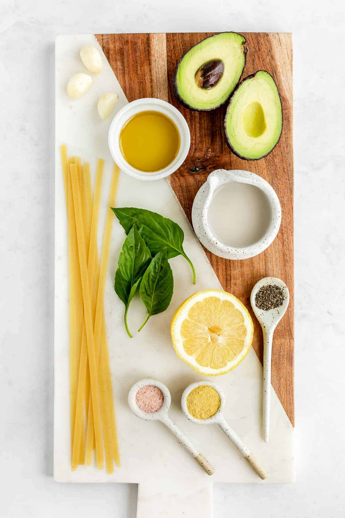 avocado, basil, garlic, olive oil, nutritional yeast, lemon juice, salt, pepper, and plant-based milk on a marble board