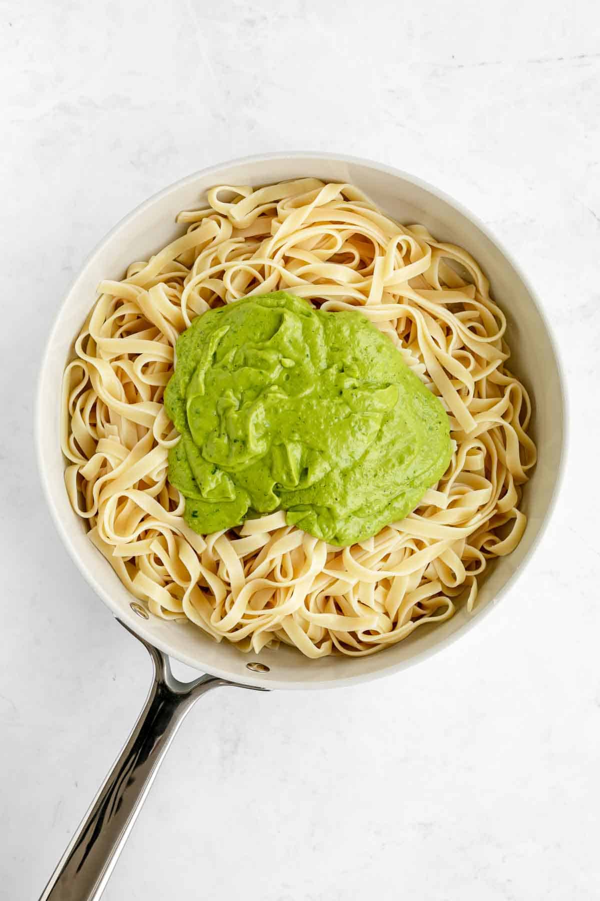 fettuccine pasta in a pot with avocado pesto sauce on top