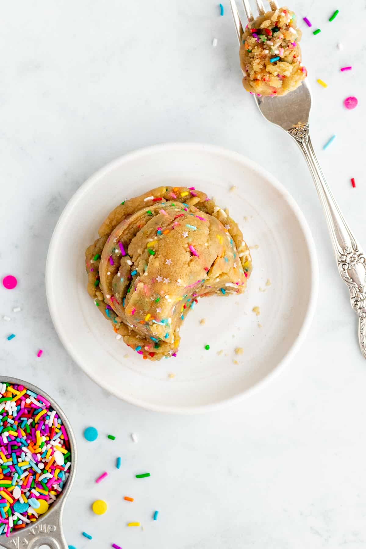 a round of edible vegan funfetti cookie dough on a small white plate with rainbow sprinkles