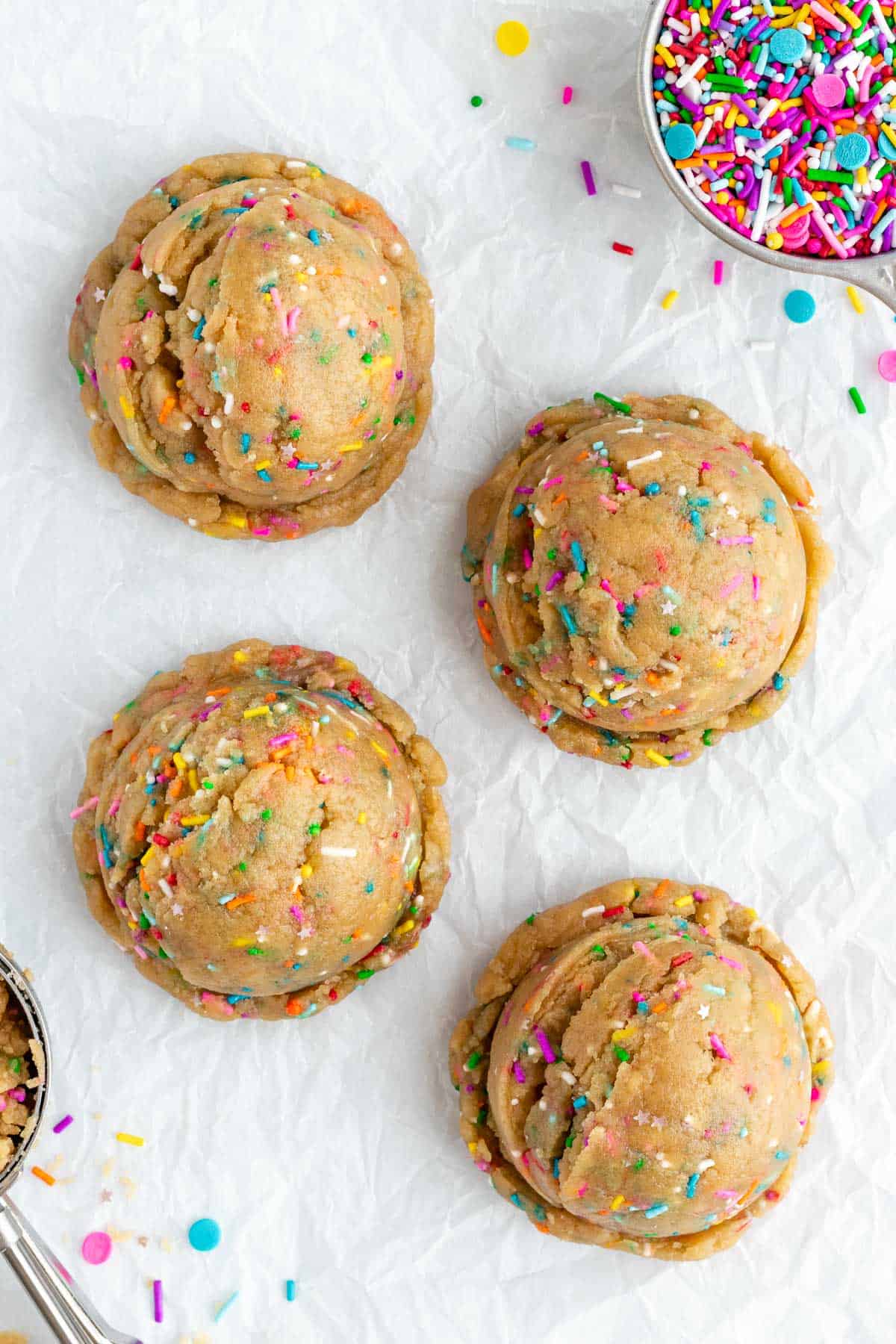four large rounds of edible funfetti cookie dough beside a bowl of vegan rainbow sprinkles
