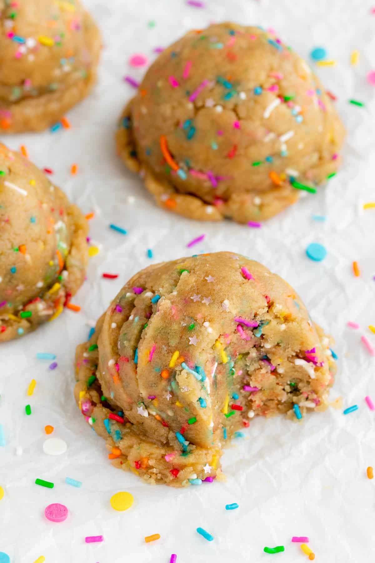 a large scoop of vegan funfetti cookie dough with a bite taken out of it surrounded by rainbow sprinkles