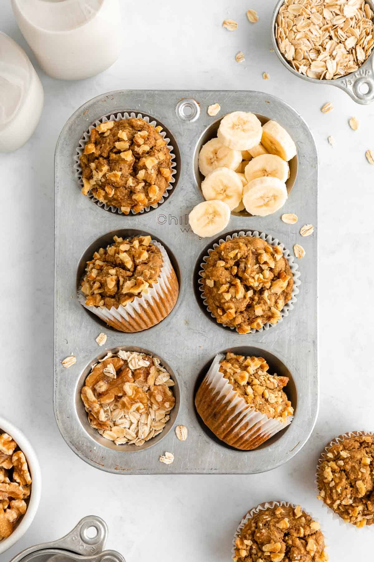 healthy banana nut muffins in a vintage muffin tin with walnuts, oats, and sliced banana