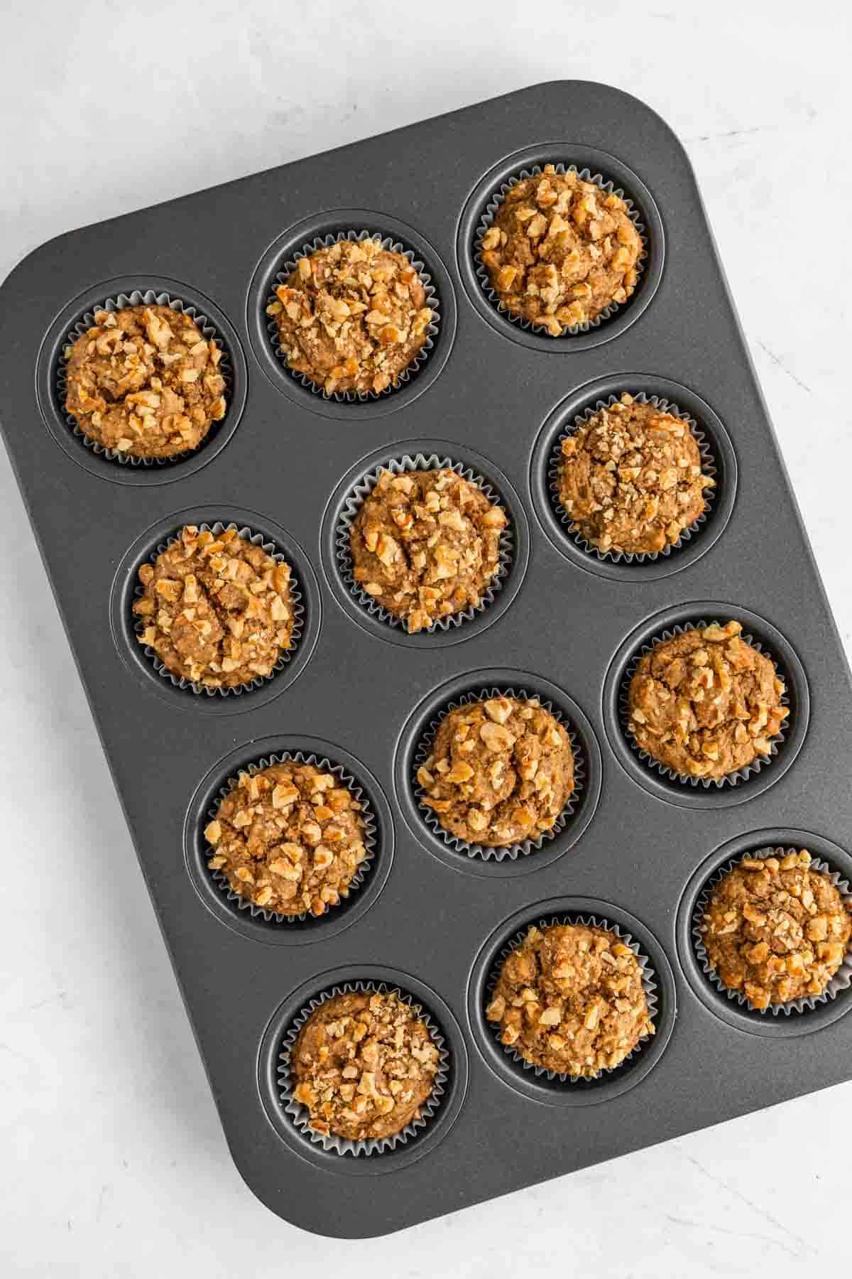 baked banana muffins in a muffin tin with walnuts on top