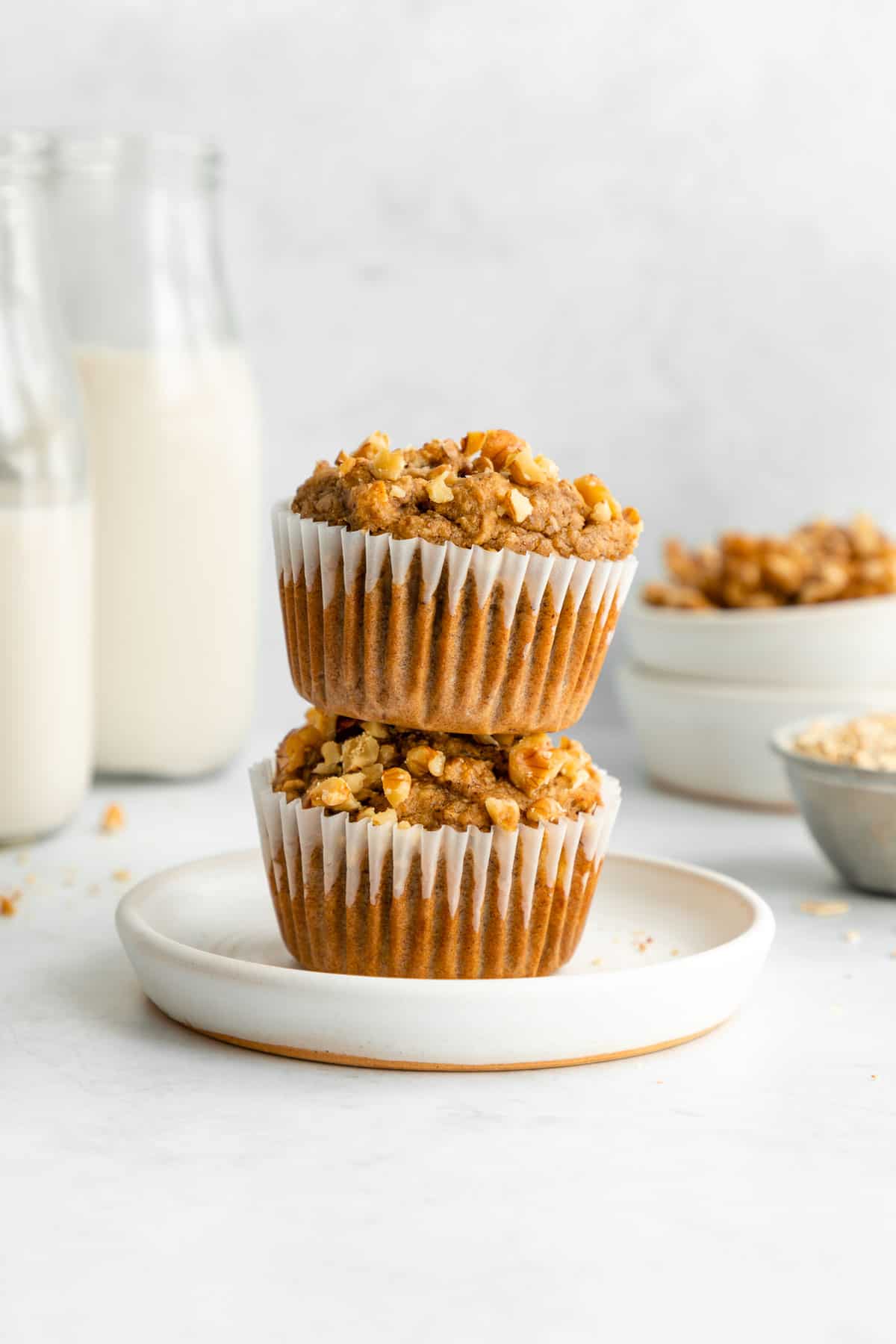 two healthy banana nut muffins stacked on a white plate beside glasses of almond milk