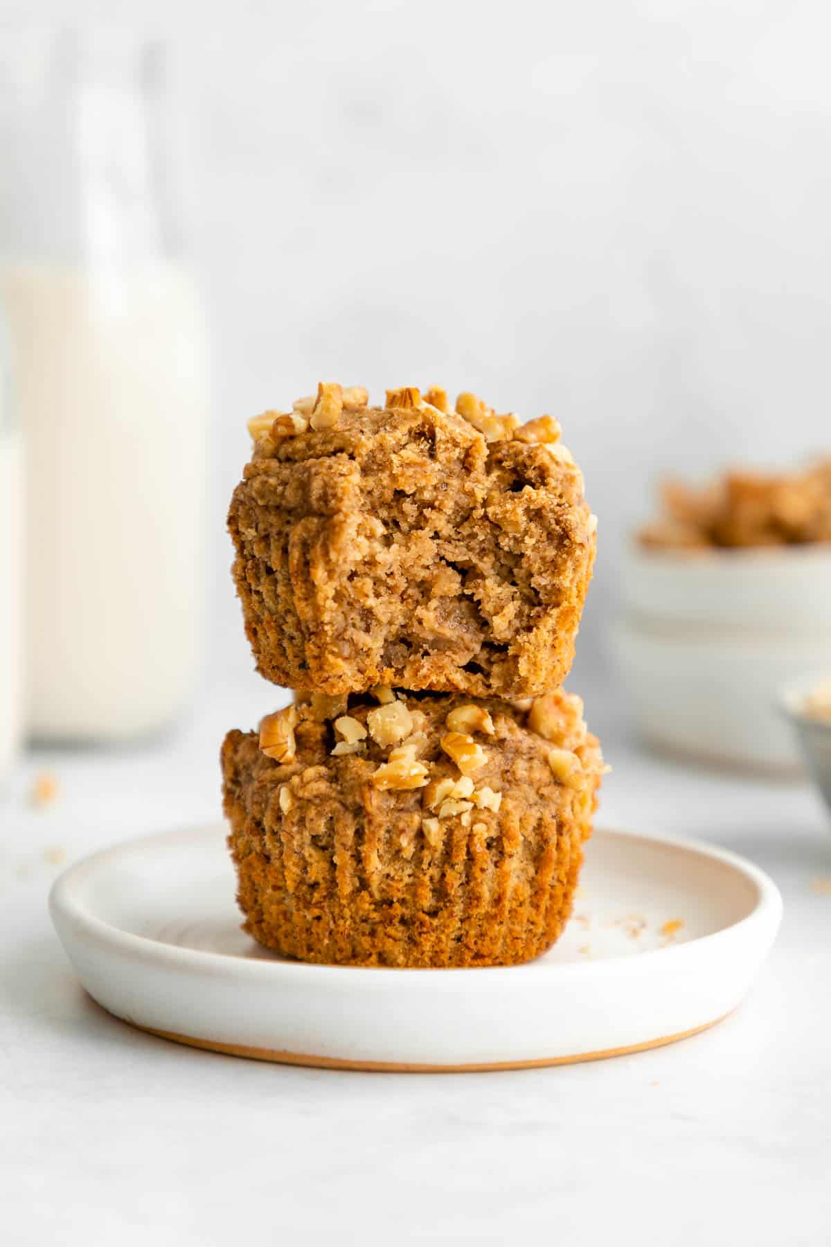 a stack of two vegan banana muffins on a white plate with a bite taken out of the top one