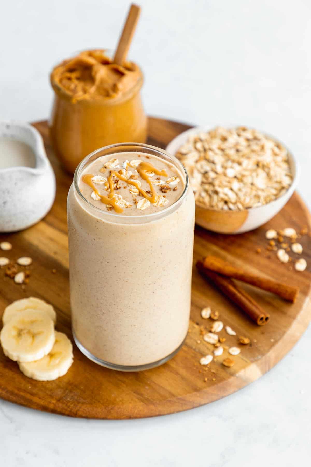 a peanut butter oatmeal smoothie bowl in a glass on top of a round wooden board