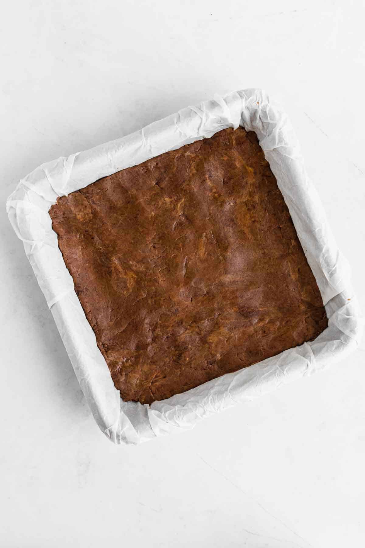 chocolate protein bar dough pressed across the bottom of a square baking dish