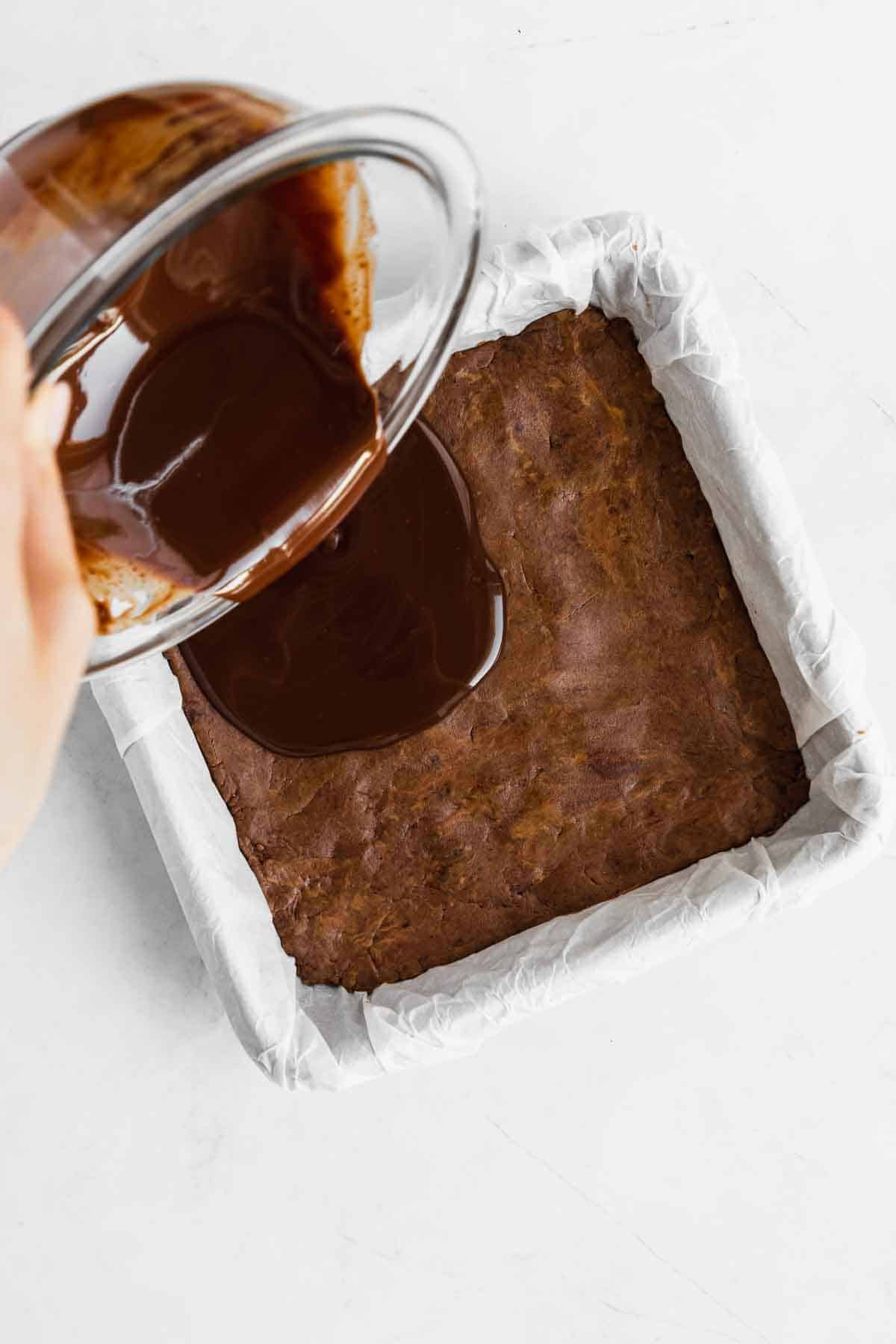 pouring melted chocolate over homemade protein bars in a square baking dish