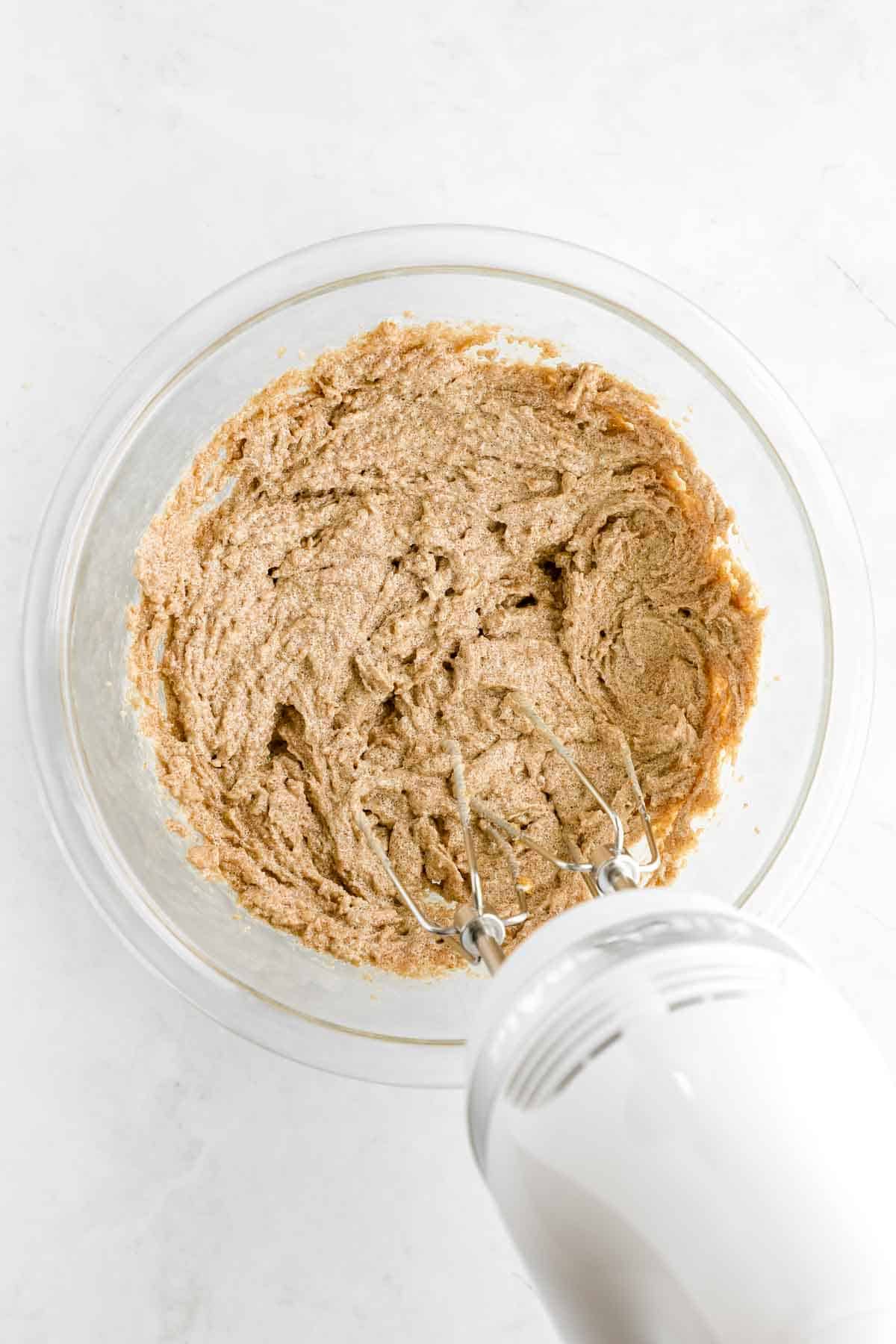 a handheld electric mixer creaming butter and sugar together in a glass bowl