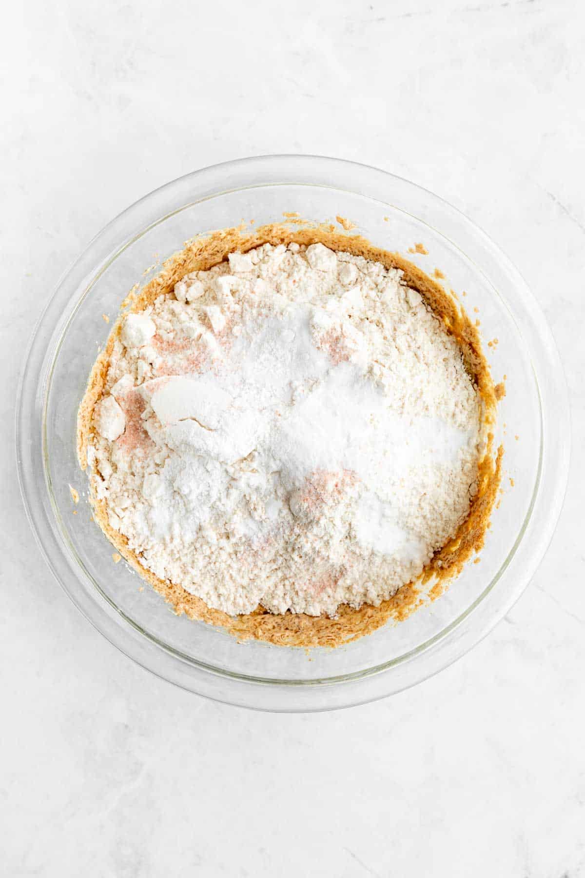 flour on top of wet cookie dough batter inside a glass bowl