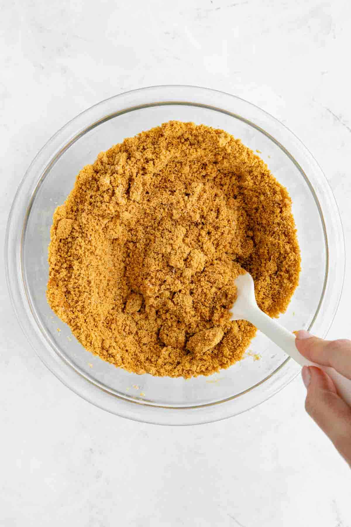 a hand mixing graham cracker crust in a glass bowl