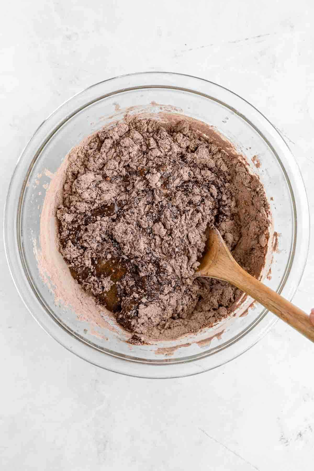 a wooden spoon mixing dry ingredients into wet ingredients for brownie batter