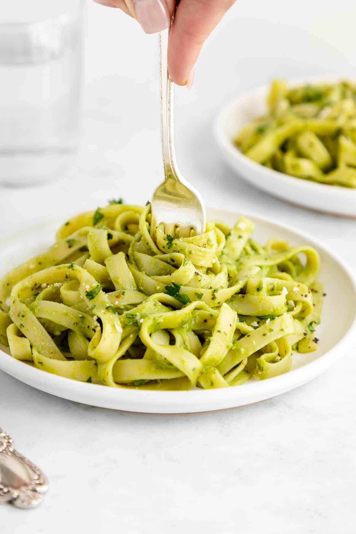 a fork twirling vegan avocado pasta on a white plate