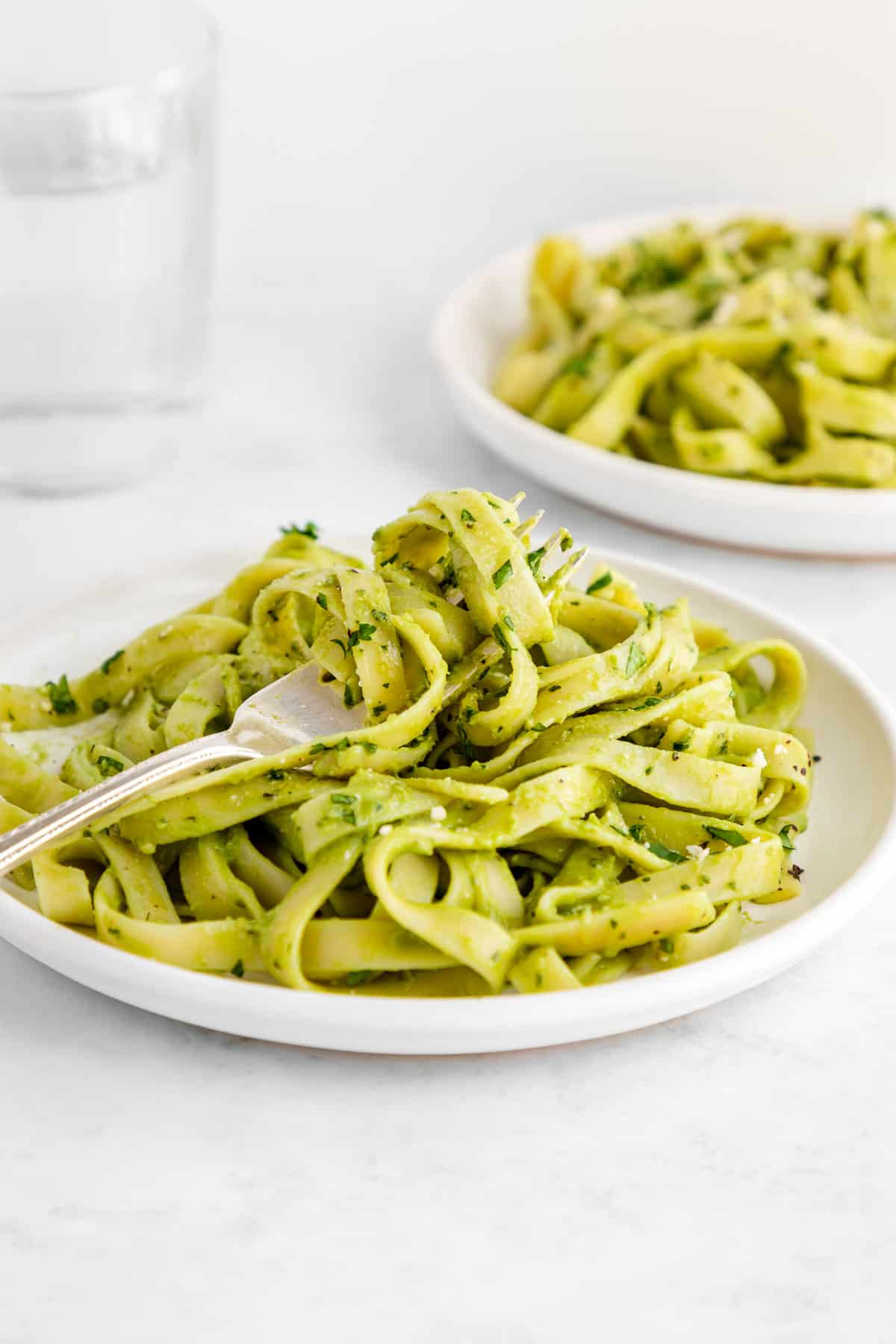 a fork twirling vegan avocado pasta on a white plate