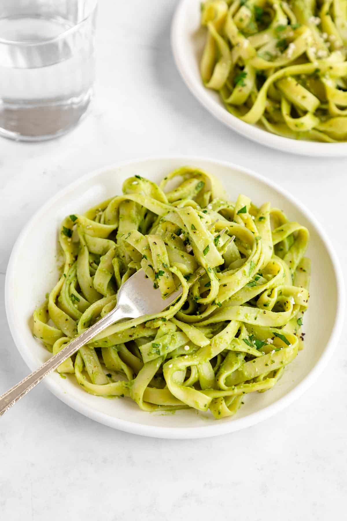 a fork twirling vegan avocado pasta on a white plate