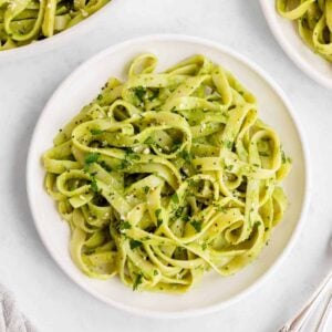 vegan avocado pasta on a white plate with basil and parmesan on top