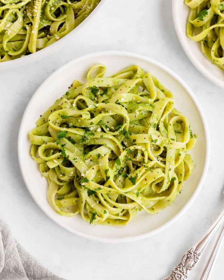 vegan avocado pasta on a white plate with basil and parmesan on top
