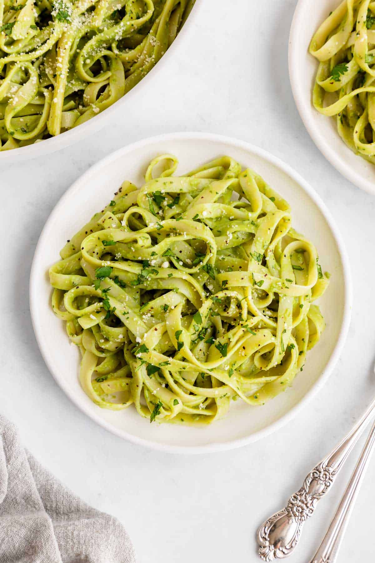 vegan avocado pasta on a white plate with basil and parmesan on top