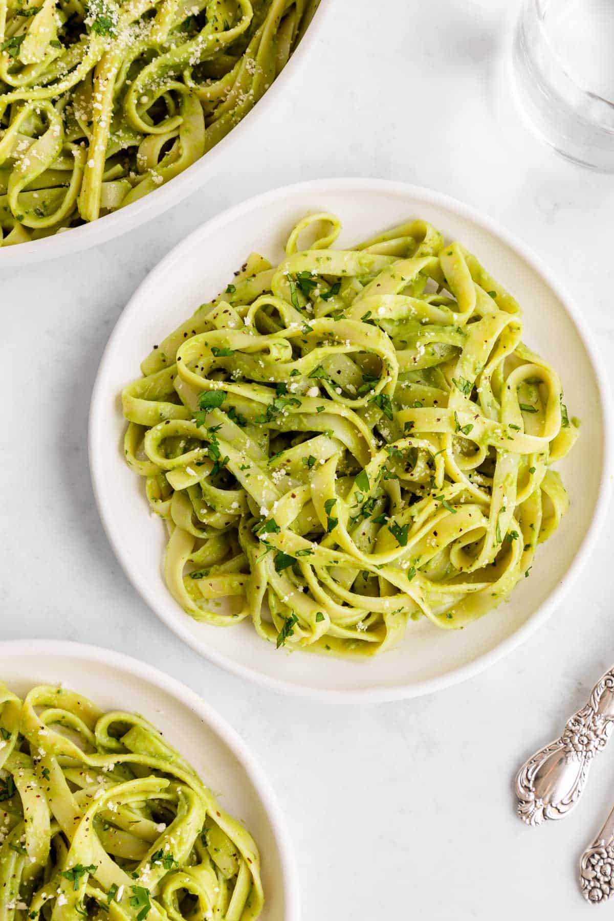 vegan avocado pasta on two white plates beside a glass of water and silverware