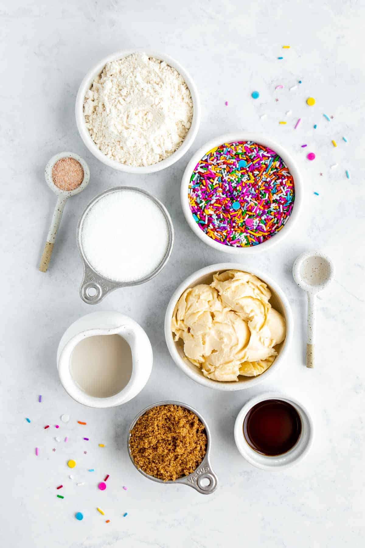 bowls filled with flour, rainbow sprinkles, vegan butter, brown sugar, white sugar, vanilla extract, almond extract, and almond milk